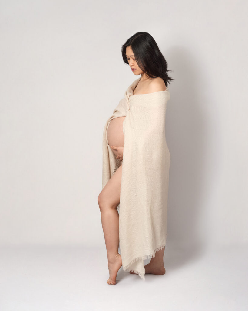 Full length pregnancy portrait in colour against a white backdrop with a cream shawl