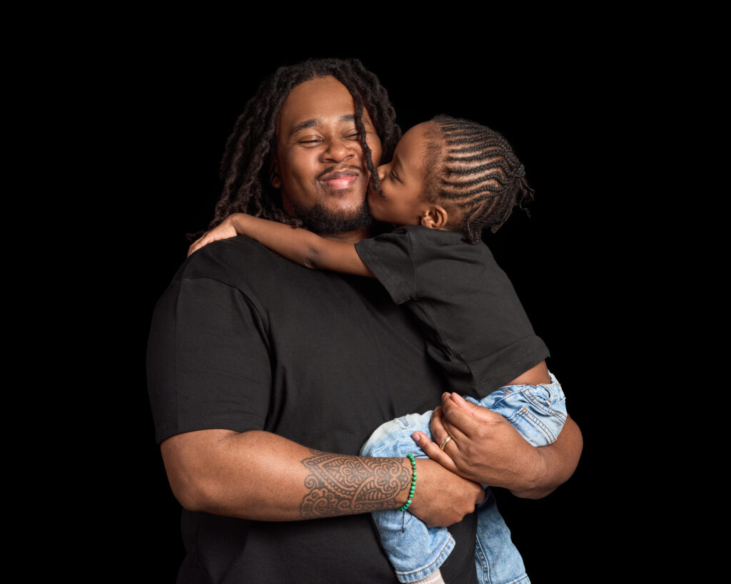 Father and son portrait by london photographer Elle Fallon. Shows son kissing his Dad.