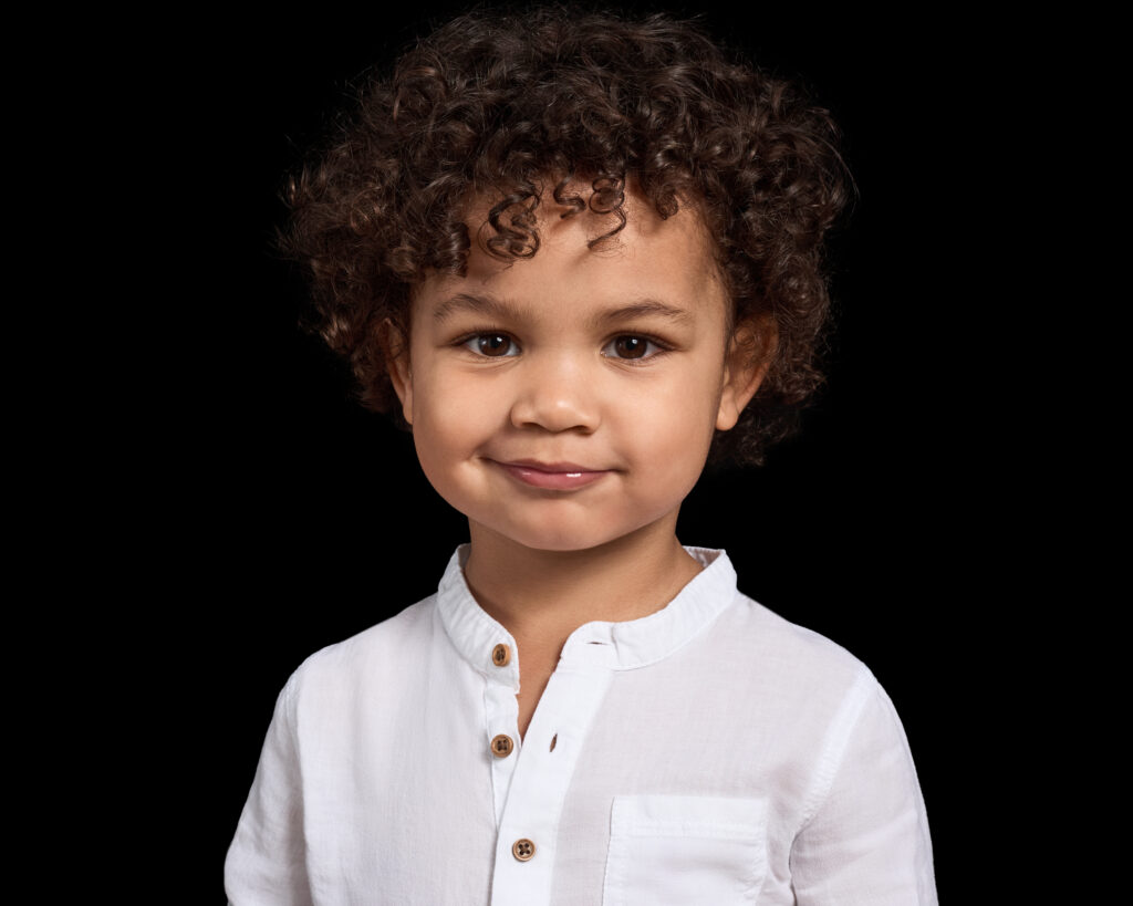 Colour portrait of a happy two-year-old boy smiling at the camera. Portrait taken in an at-home studio setting by London photographer Elle Fallon.