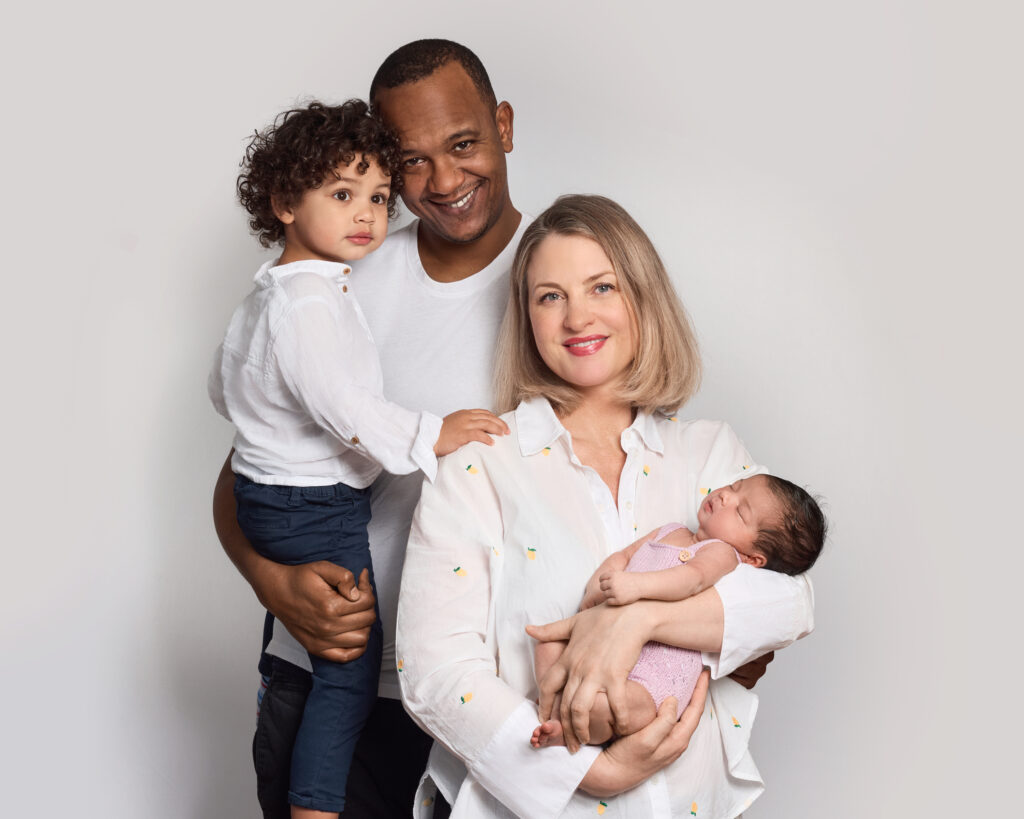 Colour family portrait taken at home with professional studio lighting. The family includes a two-year-old son and a newborn. The image feels light, fresh, and calm.