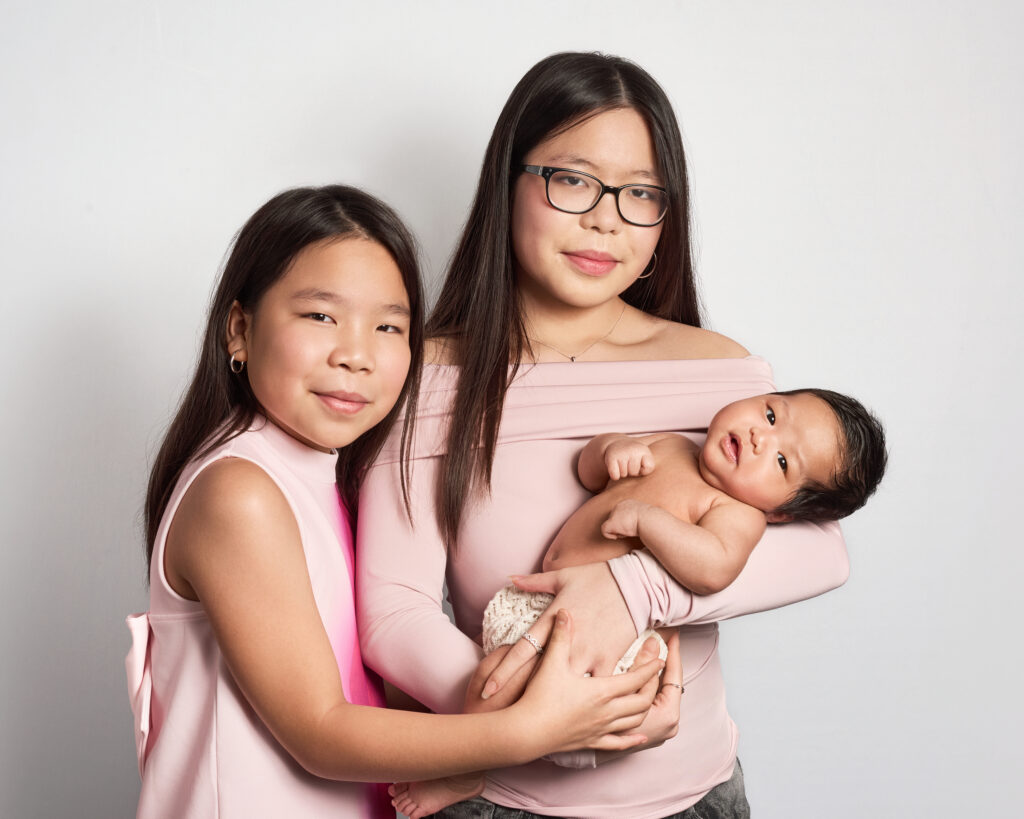 A colour portrait of two sisters holding their newborn baby sister